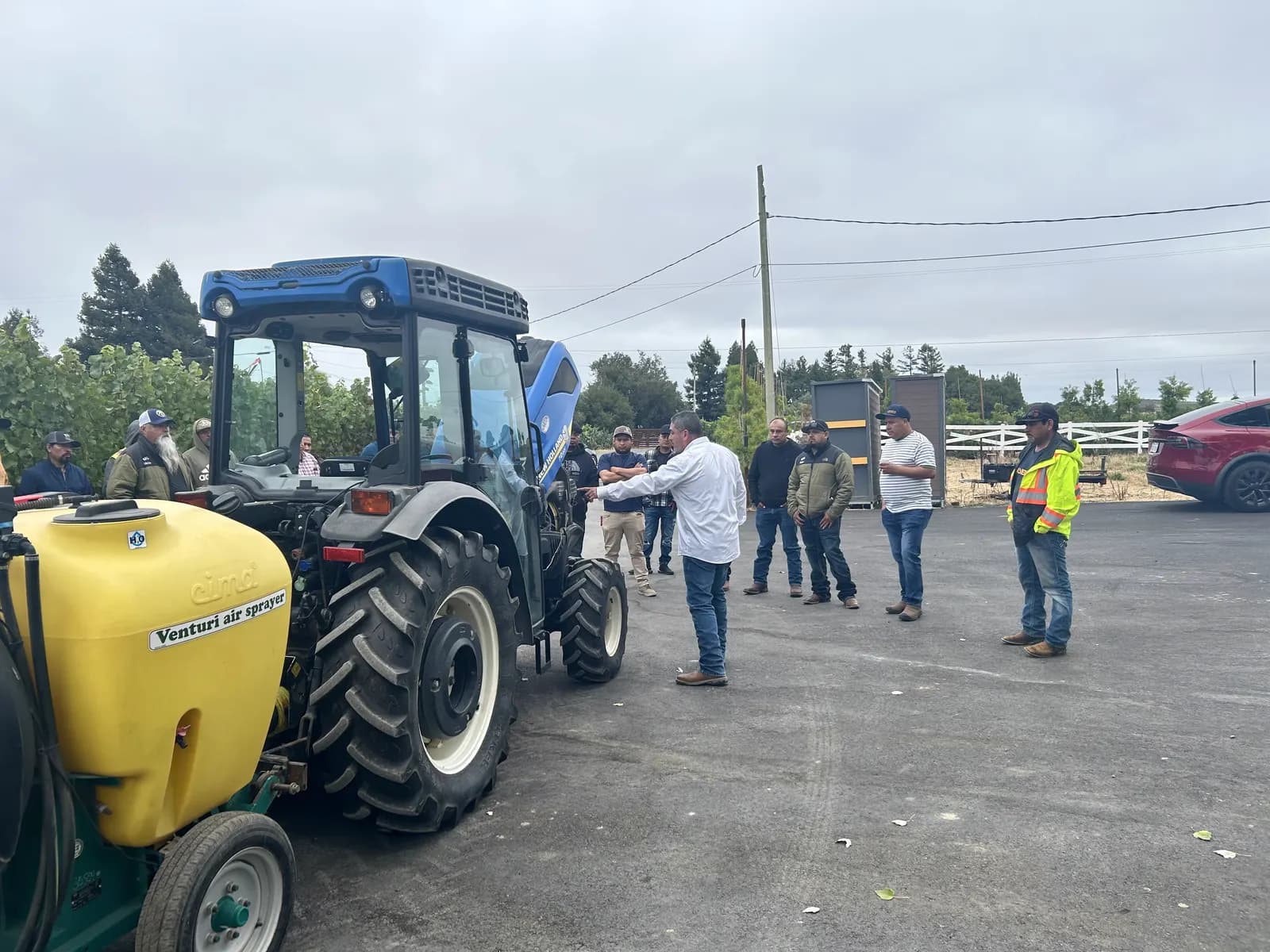 Agricultural workers gathered around a tractor and sprayer during training